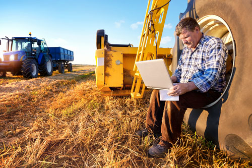 Business man sitting on tractor wheel on laptop